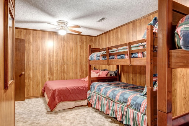 carpeted bedroom with crown molding, ceiling fan, a textured ceiling, and wooden walls