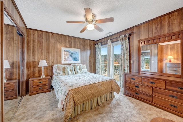 carpeted bedroom featuring ornamental molding, wooden walls, access to exterior, and a textured ceiling