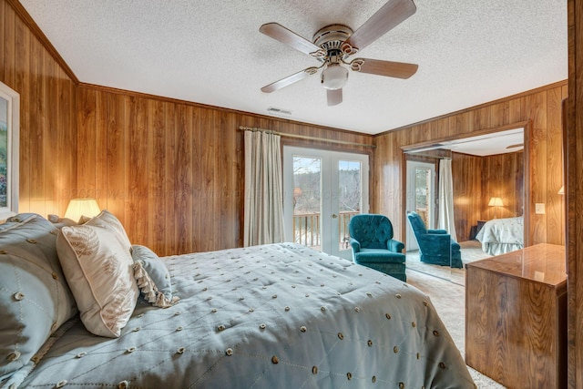 bedroom with crown molding, access to exterior, wooden walls, a textured ceiling, and french doors