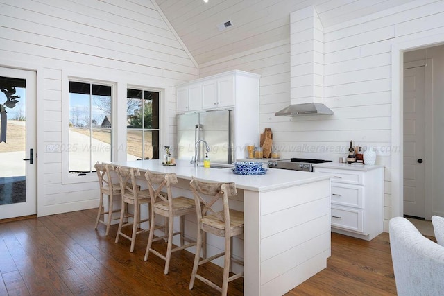 kitchen with lofted ceiling, white cabinetry, dark hardwood / wood-style floors, a center island with sink, and built in fridge