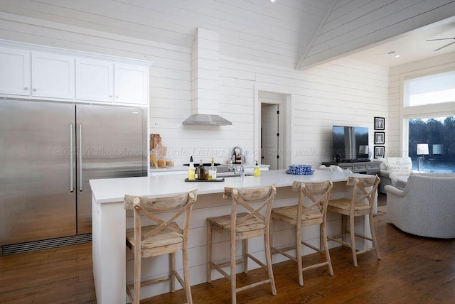 kitchen featuring a large island, built in refrigerator, a kitchen breakfast bar, white cabinets, and dark hardwood / wood-style flooring