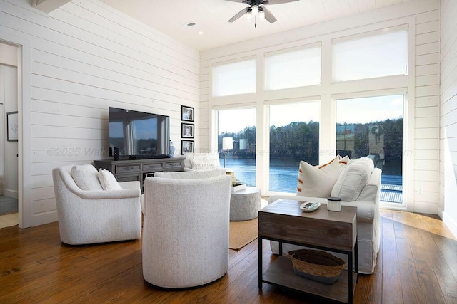 living room featuring dark wood-type flooring, a healthy amount of sunlight, a high ceiling, and wood walls