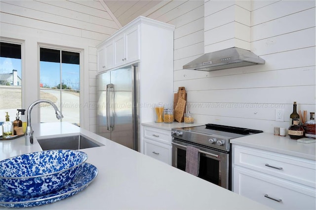 kitchen with stainless steel appliances, sink, white cabinets, and wood walls