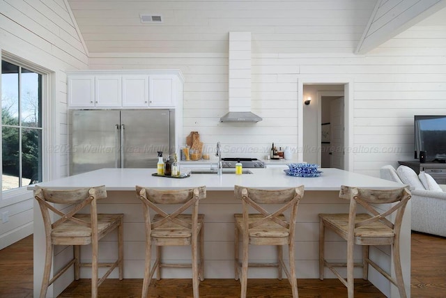 kitchen with built in refrigerator, sink, a breakfast bar area, and white cabinets