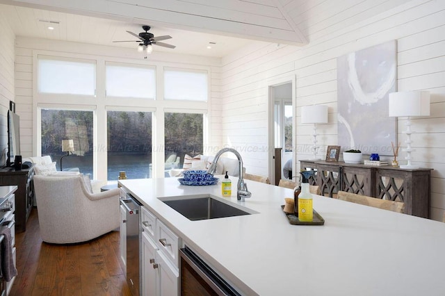 kitchen with dark hardwood / wood-style floors, sink, white cabinets, stainless steel dishwasher, and beam ceiling