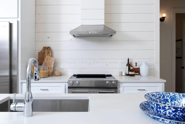 kitchen with stainless steel appliances, white cabinetry, sink, and wall chimney range hood