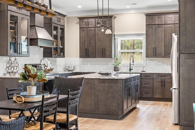 kitchen with stainless steel appliances, hanging light fixtures, sink, light stone counters, and custom exhaust hood