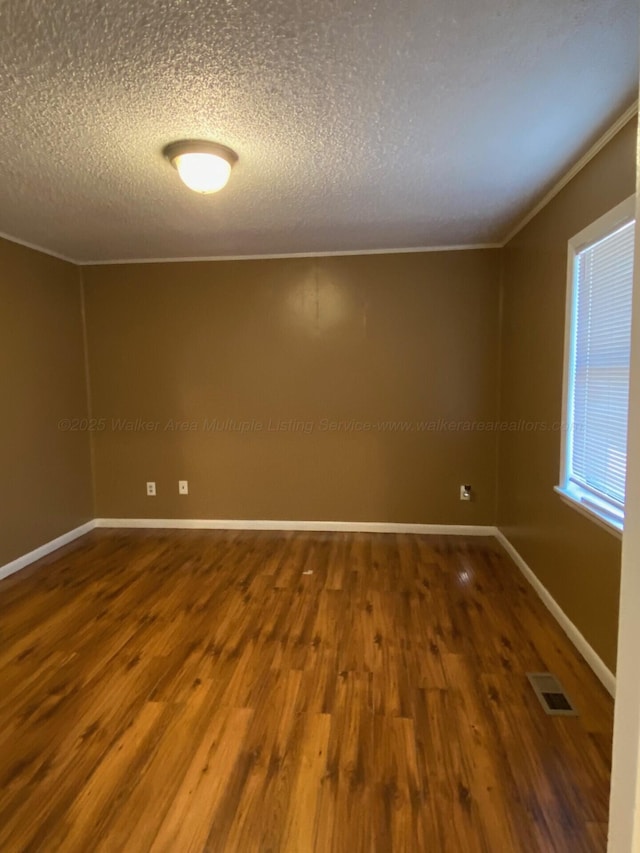 empty room featuring wood finished floors, visible vents, baseboards, ornamental molding, and a textured ceiling