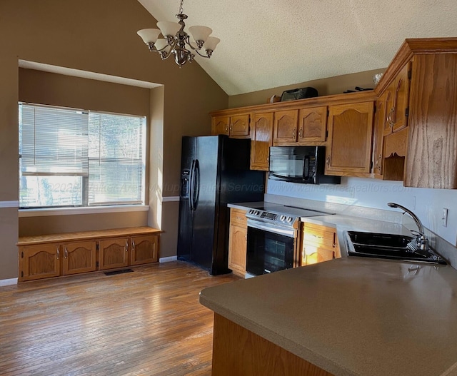 kitchen with vaulted ceiling, light wood-style floors, brown cabinetry, black appliances, and a sink