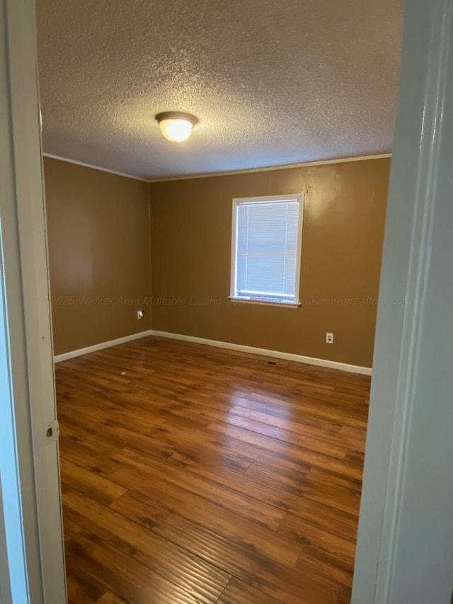 empty room featuring wood finished floors, baseboards, and a textured ceiling