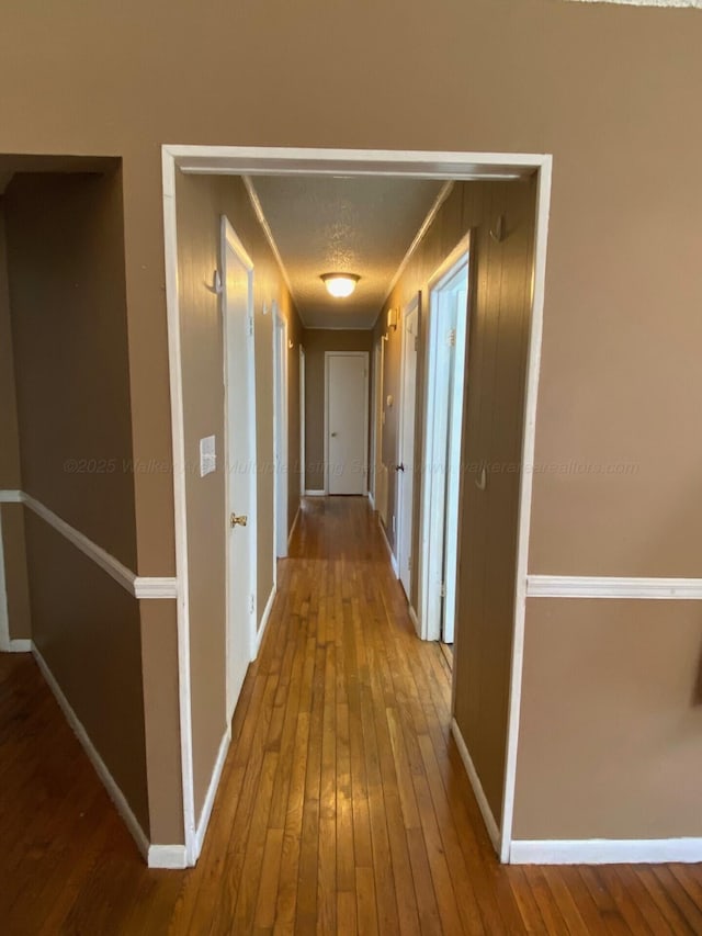 corridor featuring hardwood / wood-style flooring, baseboards, and a textured ceiling