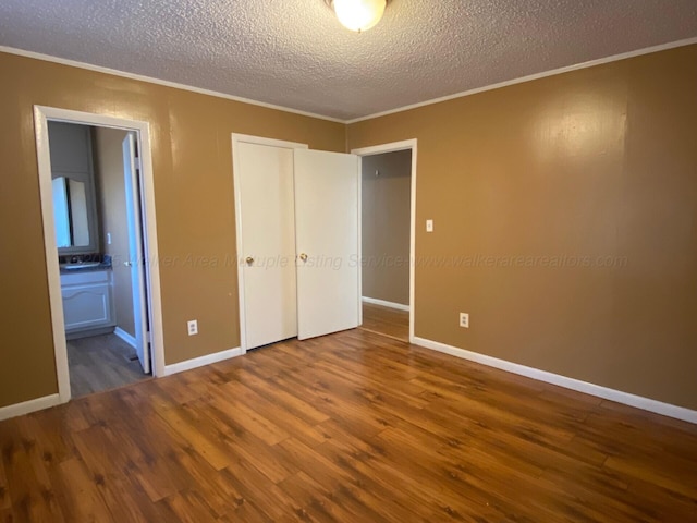 unfurnished bedroom with crown molding, wood finished floors, baseboards, and a textured ceiling