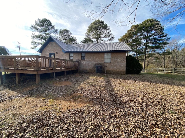 rear view of property with a deck, fence, cooling unit, metal roof, and brick siding