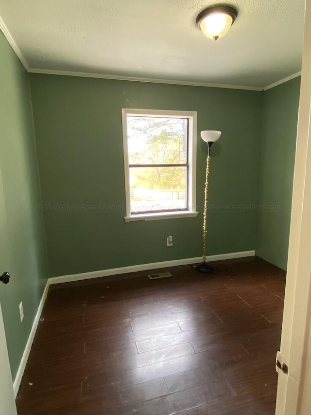 spare room with visible vents, baseboards, wood finished floors, and crown molding