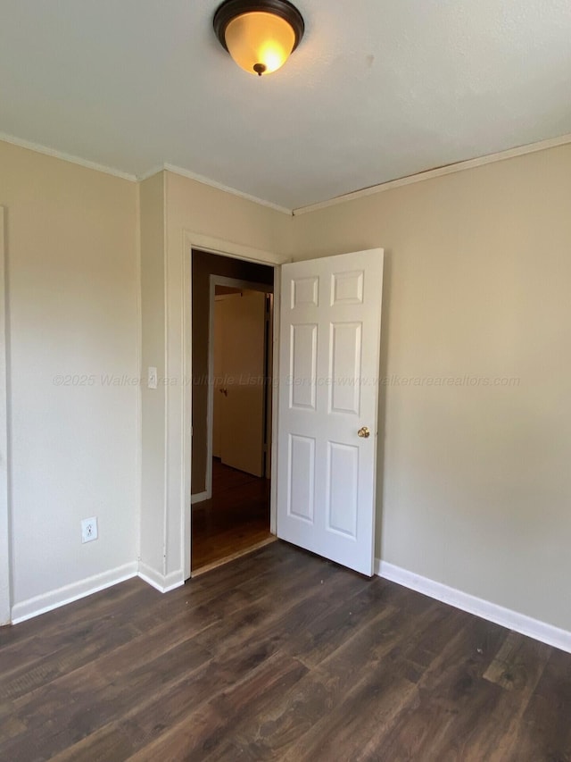 empty room with dark wood-style floors, baseboards, and ornamental molding