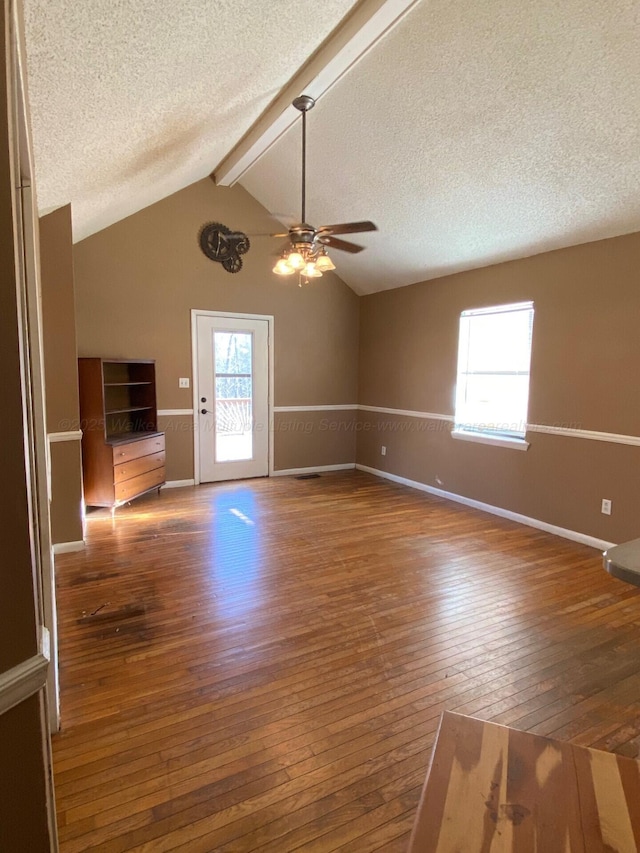 unfurnished room with hardwood / wood-style floors, a ceiling fan, baseboards, vaulted ceiling with beams, and a textured ceiling