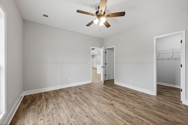 unfurnished bedroom featuring ceiling fan, a spacious closet, dark hardwood / wood-style flooring, and a closet