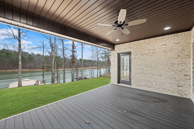 wooden terrace with a water view, ceiling fan, and a lawn