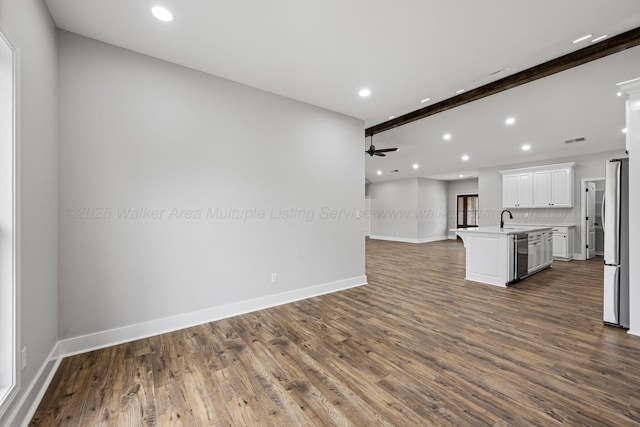 unfurnished living room featuring beamed ceiling, ceiling fan, dark hardwood / wood-style flooring, and sink