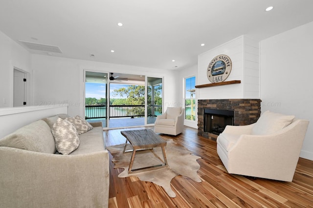 living room featuring light hardwood / wood-style floors, a stone fireplace, plenty of natural light, and ceiling fan