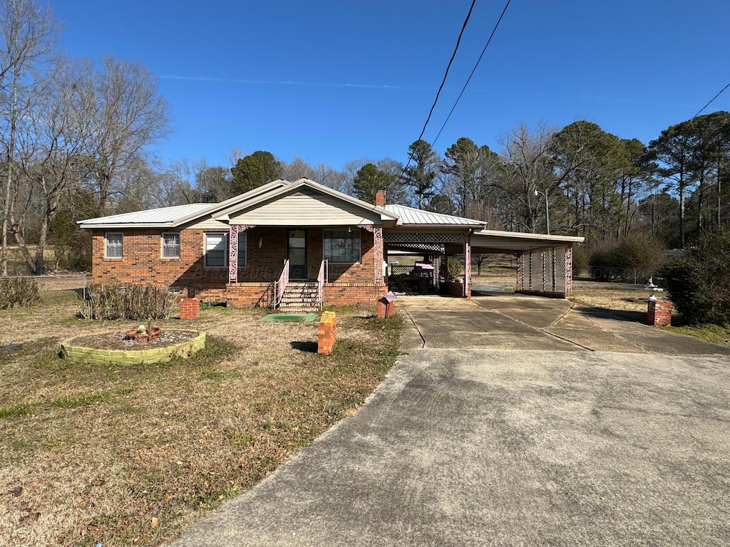 single story home featuring concrete driveway, a chimney, metal roof, a carport, and brick siding