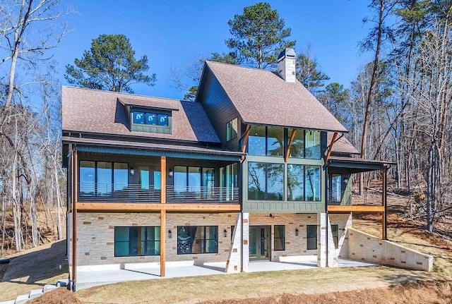 back of property featuring stone siding, a patio area, a chimney, and roof with shingles