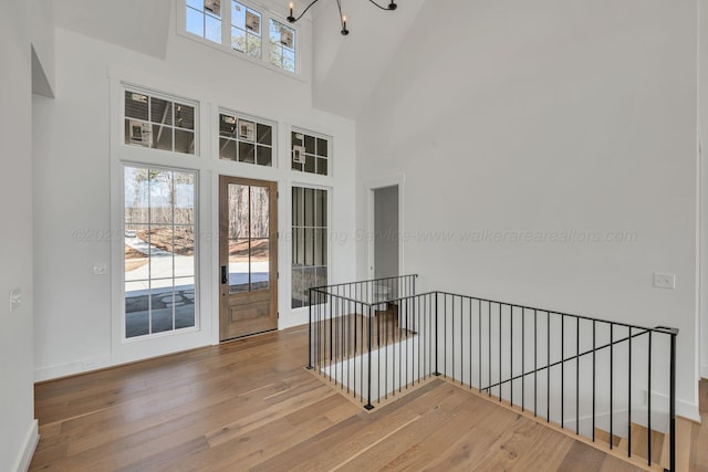 interior space featuring an inviting chandelier, wood finished floors, a towering ceiling, and baseboards