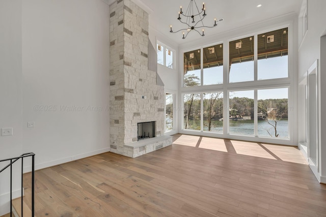 unfurnished living room featuring baseboards, wood-type flooring, an inviting chandelier, a high ceiling, and a stone fireplace