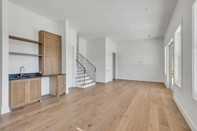 interior space featuring a sink, light wood-style flooring, baseboards, and stairs