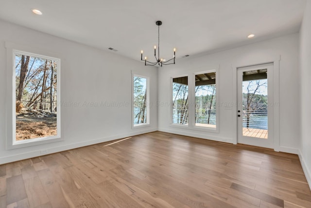 unfurnished dining area featuring baseboards, wood finished floors, and a notable chandelier