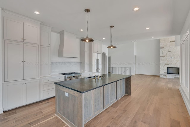 kitchen featuring light wood finished floors, dark countertops, wall chimney exhaust hood, high end stainless steel range, and a fireplace