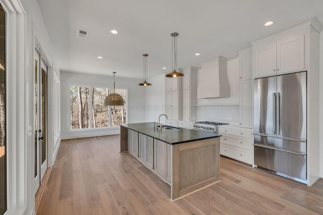 kitchen featuring high end refrigerator, a sink, visible vents, gas stove, and custom range hood