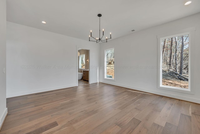 unfurnished dining area featuring a notable chandelier, baseboards, wood finished floors, and a healthy amount of sunlight