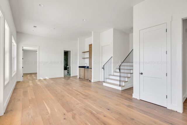 spare room with stairs, light wood finished floors, recessed lighting, and baseboards