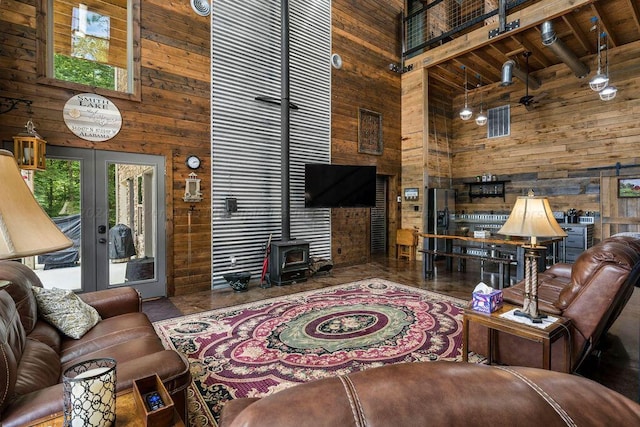 living room with french doors, a towering ceiling, wooden walls, and beam ceiling