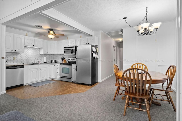 kitchen with dark tile patterned floors, stainless steel appliances, white cabinetry, and decorative light fixtures