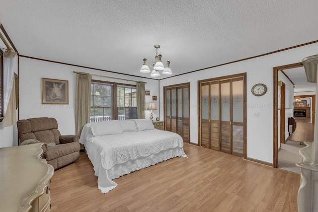 bedroom with an inviting chandelier, light hardwood / wood-style flooring, ornamental molding, and multiple closets