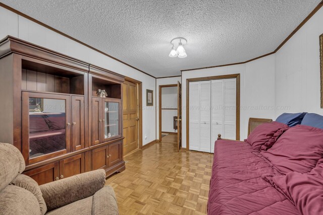 bedroom with wood walls, light parquet floors, ornamental molding, a textured ceiling, and a closet