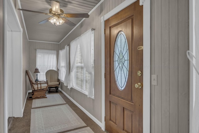 foyer with crown molding, ceiling fan, and dark colored carpet