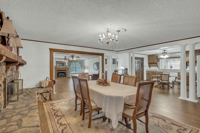 dining room with light hardwood / wood-style flooring, ornamental molding, a textured ceiling, and ornate columns