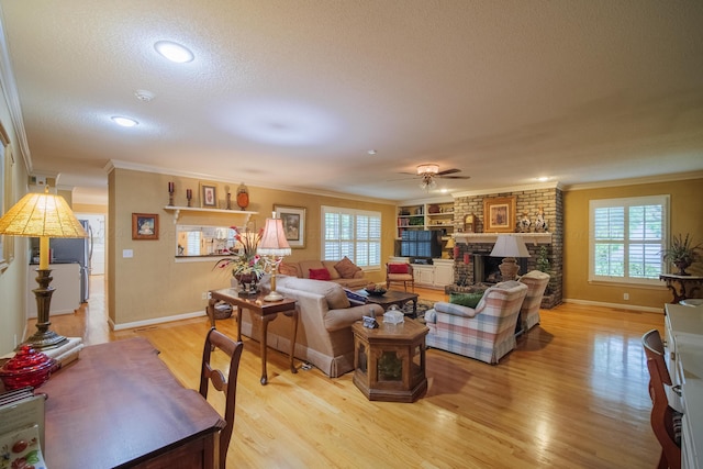 living room featuring ceiling fan, light wood-type flooring, a fireplace, ornamental molding, and a textured ceiling