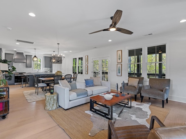 living room featuring ceiling fan with notable chandelier, light wood-type flooring, ornamental molding, and french doors