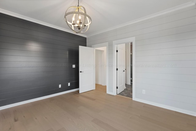 unfurnished bedroom with wood walls, ornamental molding, wood-type flooring, and a notable chandelier