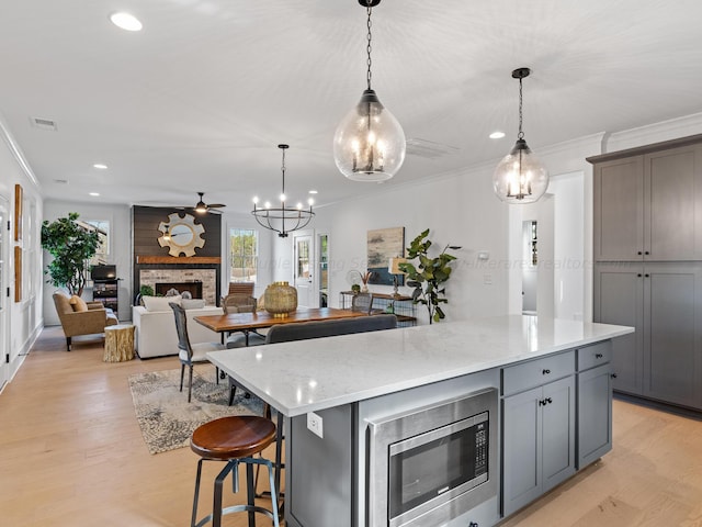 kitchen with ornamental molding, stainless steel microwave, hanging light fixtures, and light hardwood / wood-style flooring