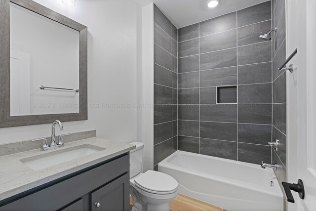 full bathroom featuring vanity, wood-type flooring, tiled shower / bath combo, and toilet