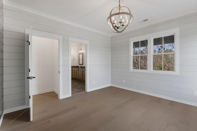 unfurnished bedroom featuring ornamental molding, wooden walls, an inviting chandelier, hardwood / wood-style floors, and connected bathroom