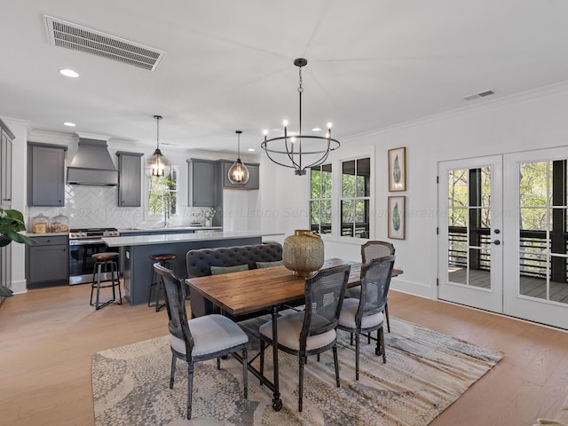 dining area featuring french doors, an inviting chandelier, ornamental molding, and light wood-type flooring