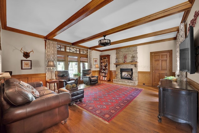 living room with beam ceiling, a stone fireplace, wood-type flooring, and crown molding