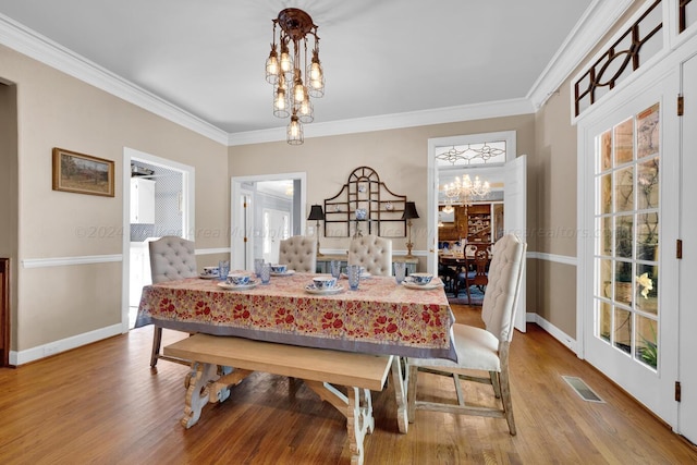 dining area featuring wood-type flooring, ornamental molding, and a notable chandelier