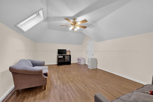 sitting room with hardwood / wood-style flooring, ceiling fan, and vaulted ceiling with skylight